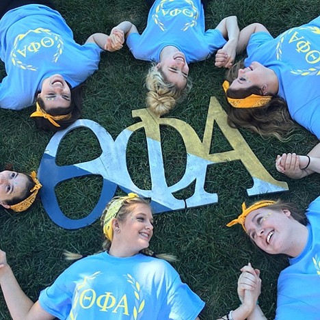 members in a circle around letters holding hands laying on grass