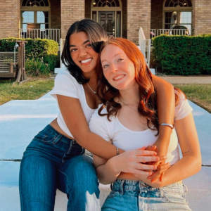 two members sitting in front of house hugging and smiling